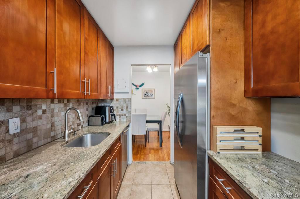 196-72 69th Avenue, Unit 1 Queens, NY 11365 - Photo 12 of 23 Kitchen featuring appliances with stainless steel finishes, light stone countertops, brown cabinets, and tasteful backsplash
