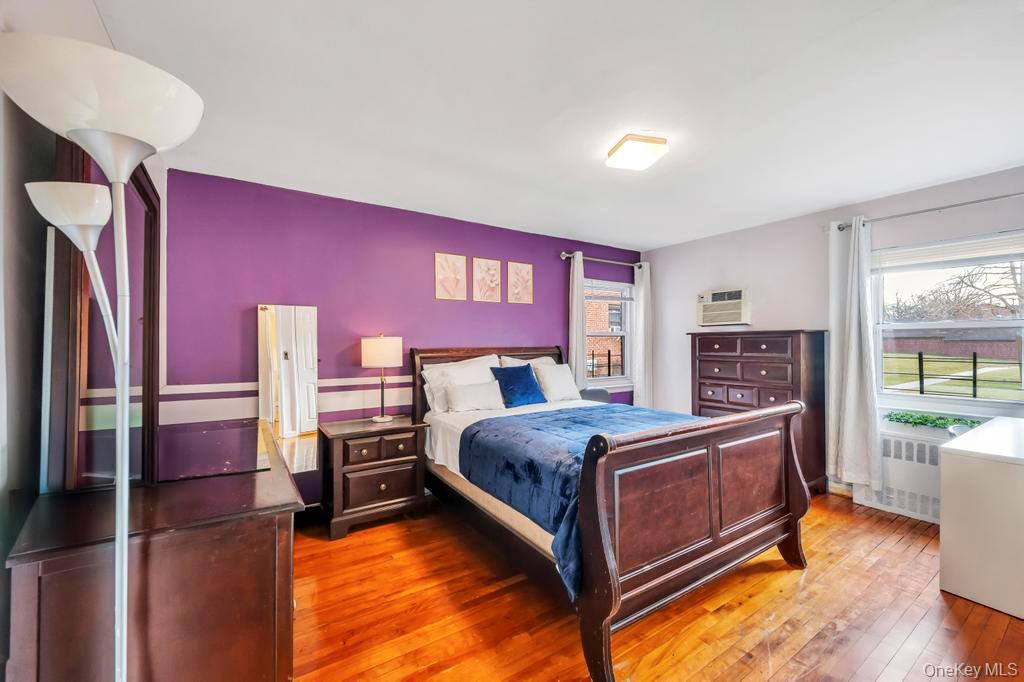 196-72 69th Avenue, Unit 1 Queens, NY 11365 - Photo 13 of 23 Bedroom featuring multiple windows, wood-type flooring, a wall unit AC, and radiator heating unit