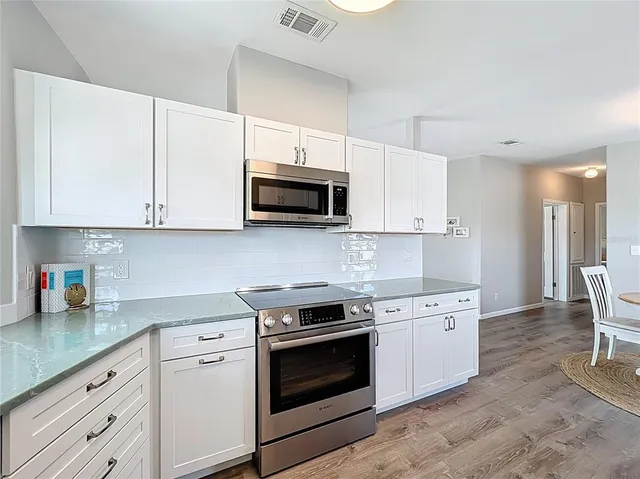 a kitchen with stainless steel appliances granite countertop a stove top oven a sink dishwasher a dining table and chairs with wooden floor