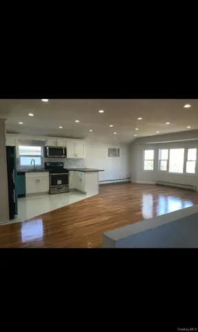 a view of an empty room with kitchen natural light and wooden floor