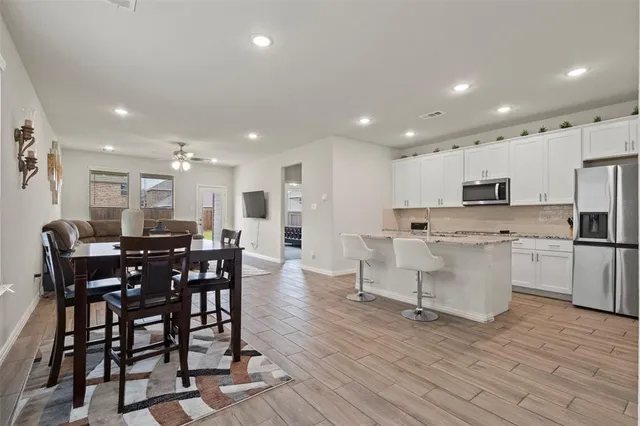 a kitchen with stainless steel appliances kitchen island granite countertop a dining table chairs and white cabinets