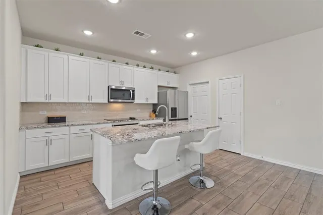 a kitchen with kitchen island granite countertop a sink a stove a refrigerator cabinets and chairs