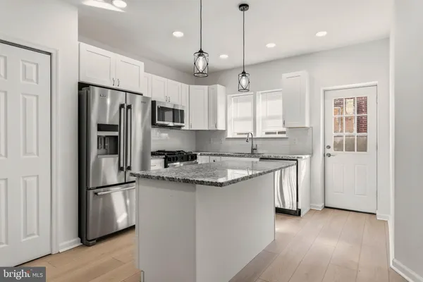 a kitchen with stainless steel appliances granite countertop a refrigerator a sink dishwasher a stove and white cabinets with wooden floor