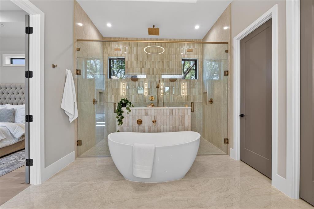11028 Edgemere Road Dallas, TX 75230 - Photo 27 of 40 Freestanding soaking tub with gold-tone fixtures, surrounded by a glass-enclosed shower with vertical tile accents
