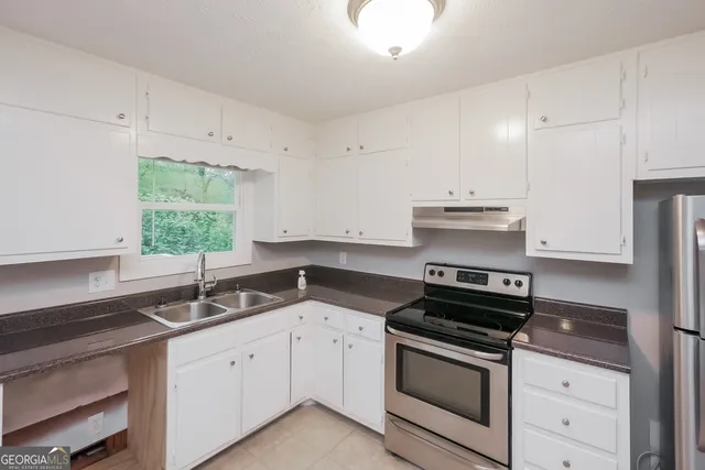 a kitchen with granite countertop white cabinets appliances a sink and a window