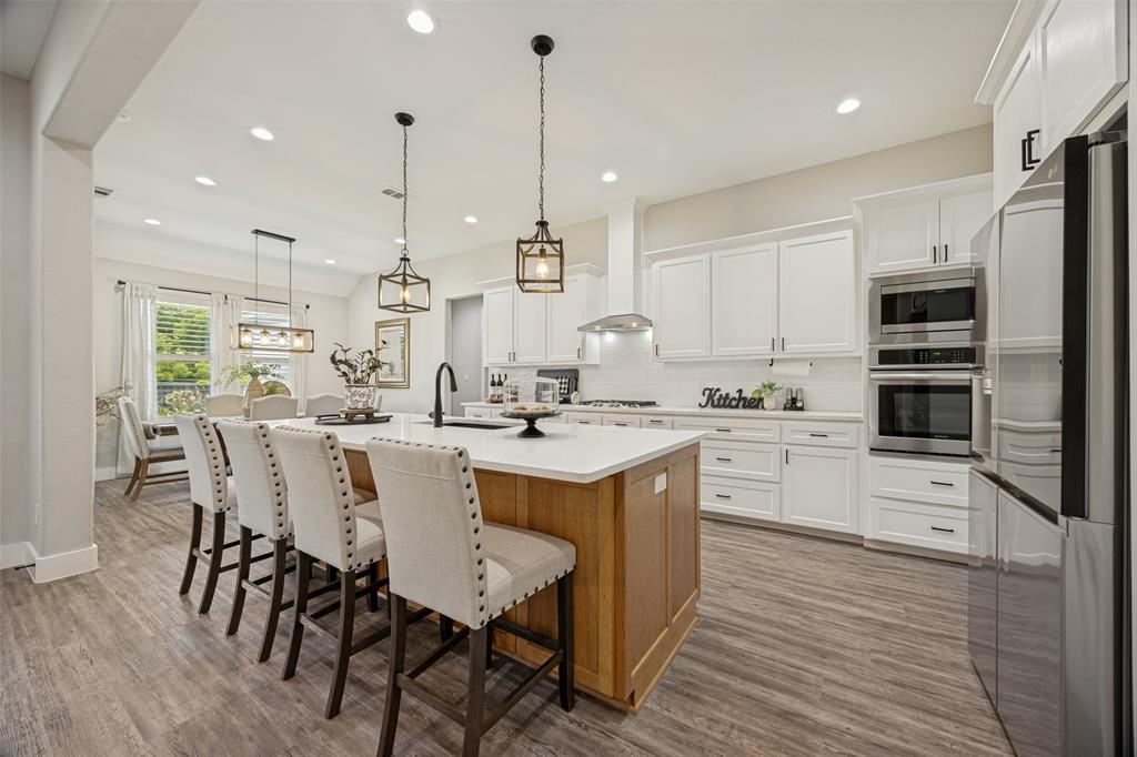 1105 Ranch Drive Bonham, TX 75418 - Photo 5 of 25 Open-concept kitchen featuring an oversized island with seating, wood-finish flooring, white cabinetry, integrated stainless steel appliances, and ceiling-mounted light fixtures