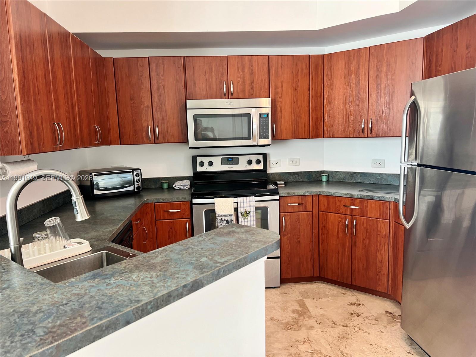 9172 Collins Avenue, Unit 305 Surfside, FL 33154 - Photo 8 of 37 a kitchen with granite countertop wooden cabinets and stainless steel appliances