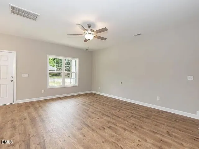 an empty room with wooden floor fan and windows