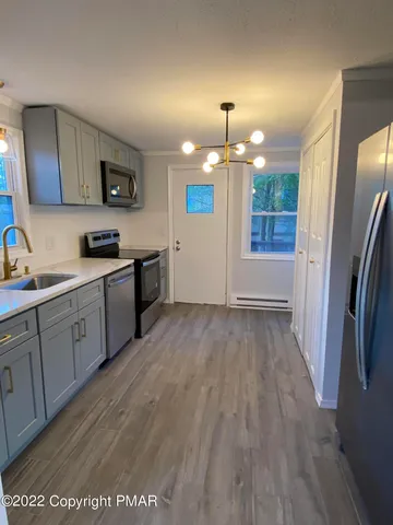 a view of a kitchen with stainless steel appliances granite countertop a refrigerator a sink dishwasher a stove and white countertops with wooden floor