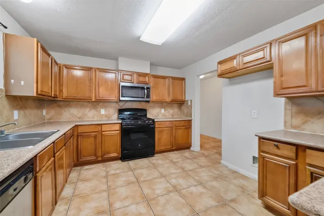 a kitchen with stainless steel appliances granite countertop a stove top oven a sink dishwasher and a refrigerator with wooden cabinets