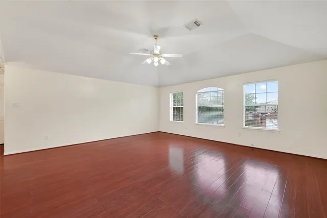 an empty room with wooden floor chandelier fan and windows