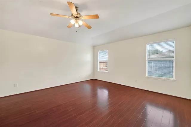 an empty room with wooden floor fan and windows