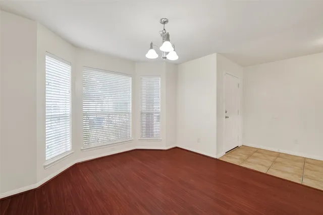 an empty room with wooden floor chandelier fan and windows