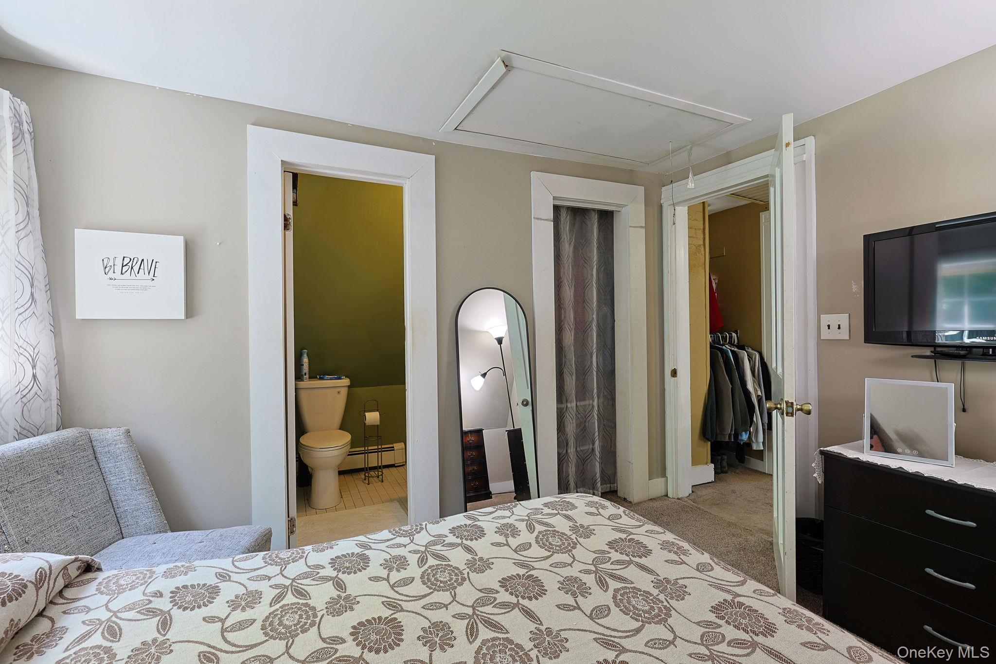 9 Library Road Tuxedo Park, NY 10987 - Photo 23 of 37 Bedroom featuring a window with sheer curtains, a built-in closet with carpet flooring, and an en-suite bathroom with a toilet and white tile flooring