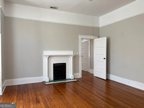 a view of an empty room with wooden floor fireplace and a window