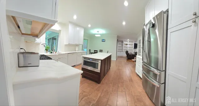 a kitchen with stainless steel appliances granite countertop a refrigerator a sink dishwasher a stove and a dining table with wooden floor