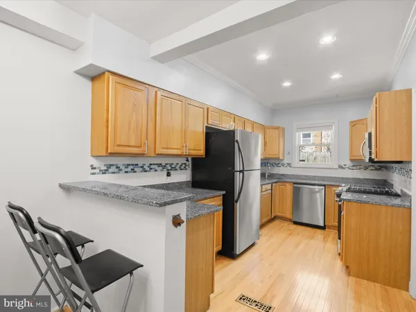 a kitchen with stainless steel appliances granite countertop a refrigerator a sink dishwasher a stove with chairs and wooden floor