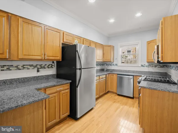 a kitchen with granite countertop a refrigerator a stove a sink dishwasher and wooden cabinets with wooden floor