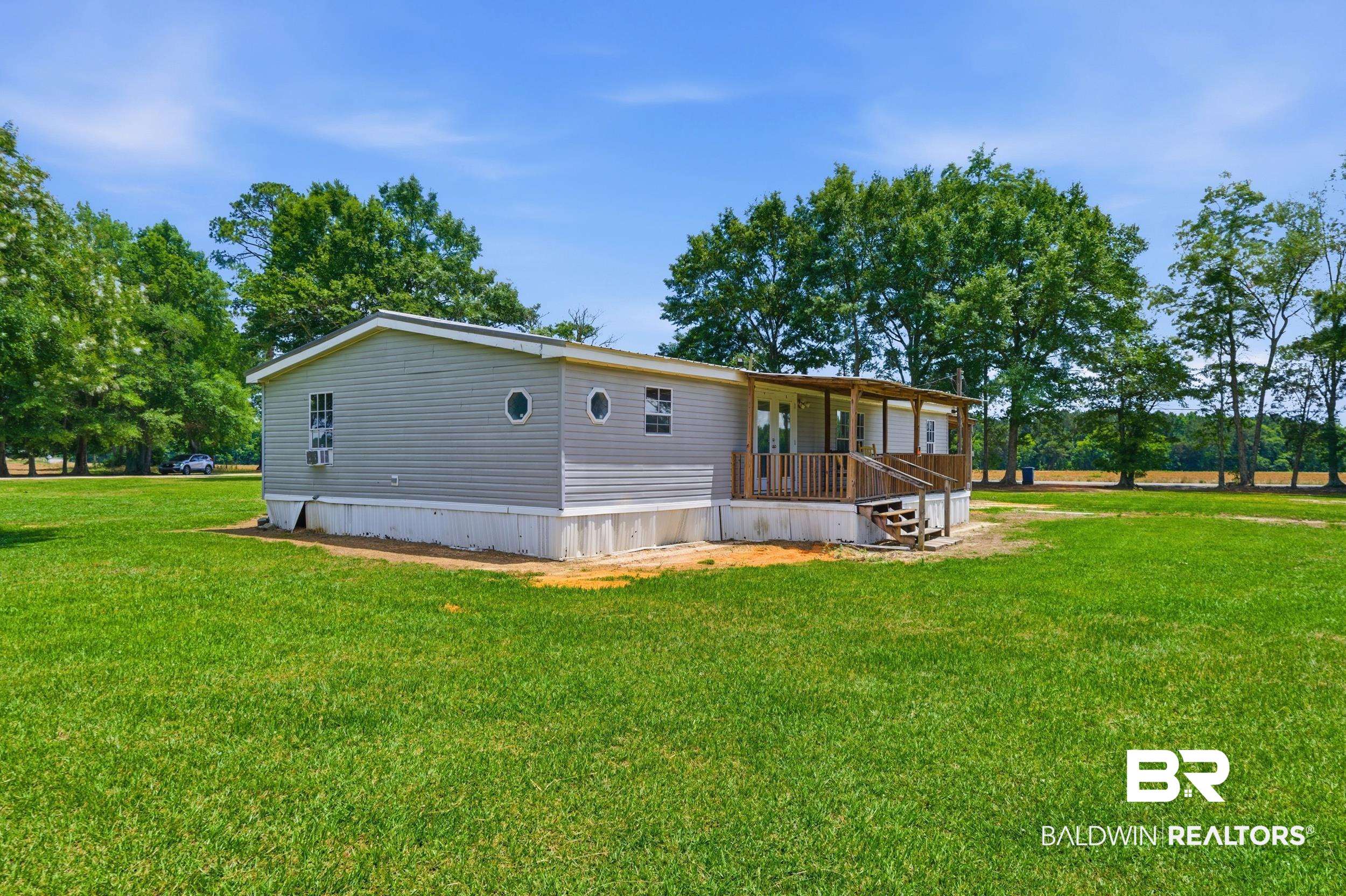 926 Tumbling Lane Atmore, AL 36502 - Photo 43 of 56 Spacious exterior with light gray horizontal siding, a covered wooden porch, and an expansive lawn