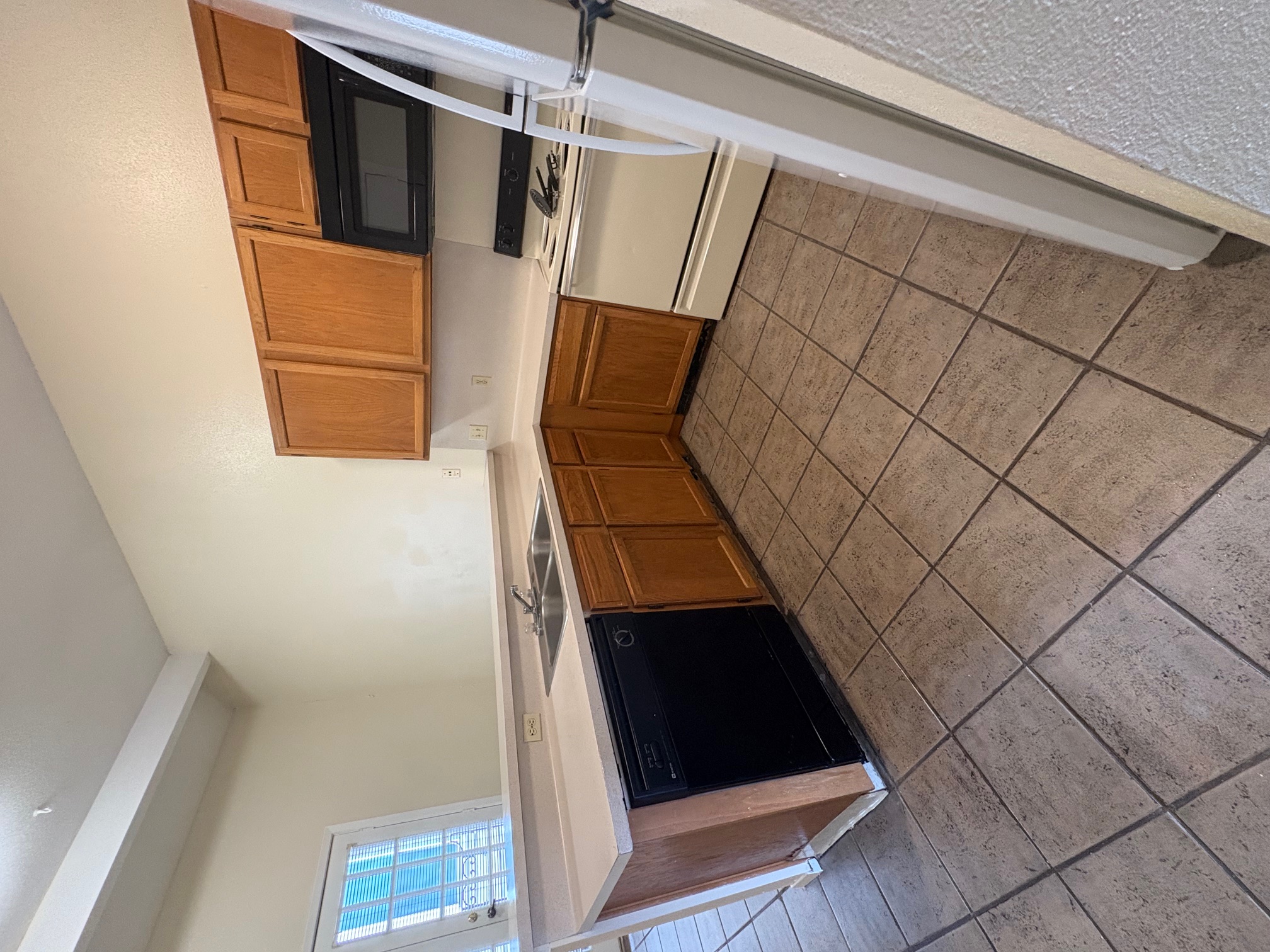 2801 Rio Grande Street, Unit 303 Austin, TX 78705 - Photo 6 of 11 Kitchen featuring black appliances, light countertops, brown cabinetry, a peninsula, and tile patterned flooring
