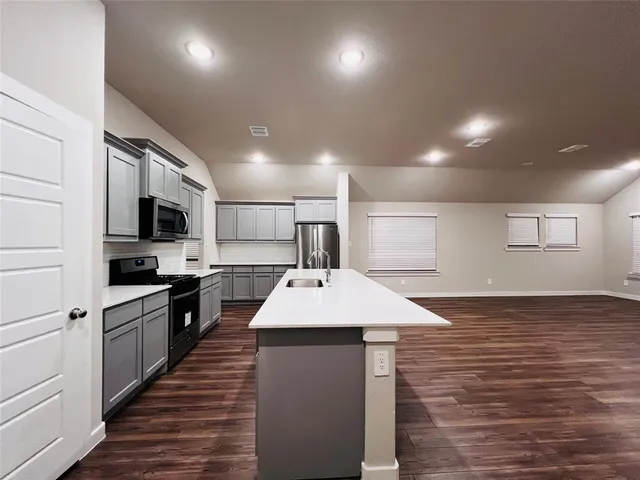 a room with stainless steel appliances kitchen island a sink dishwasher a stove and a refrigerator with wooden floor