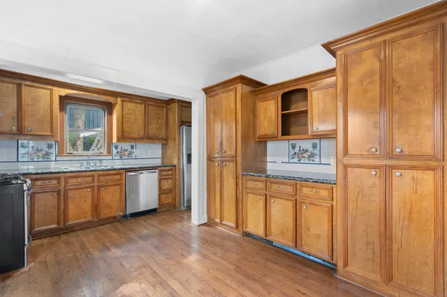 a kitchen with stainless steel appliances granite countertop a refrigerator a sink dishwasher and wooden cabinets with wooden floor