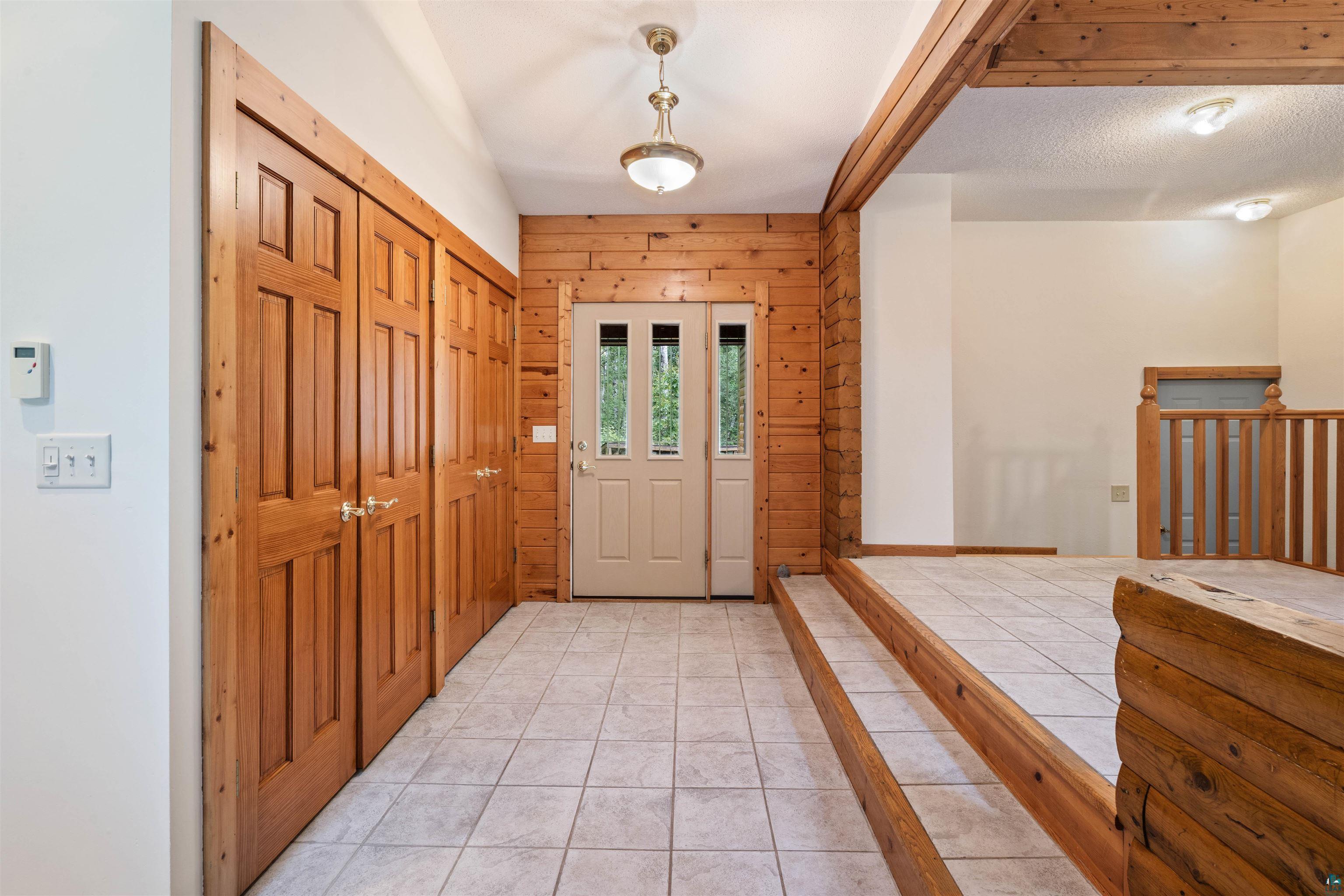 5373 Lester River Road Duluth, MN 55804 - Photo 10 of 39 Entryway with tiled flooring, wood-paneled walls, a wood-paneled door with sidelights, and two sets of wood bi-fold doors