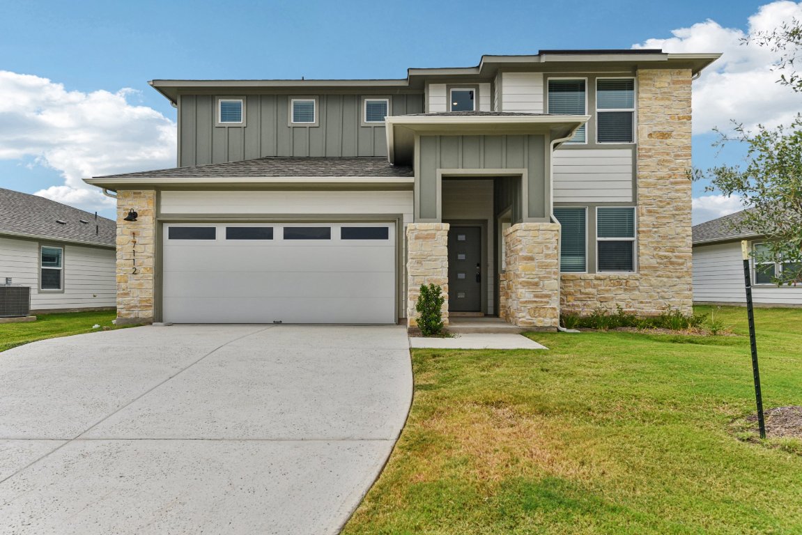 View of front facade featuring stone siding, board and batten siding, a garage, and driveway