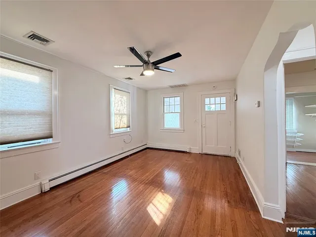 an empty room with wooden floor chandelier fan and windows