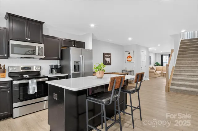 a kitchen with stainless steel appliances granite countertop a stove a sink a microwave a refrigerator with white cabinets and wooden floor