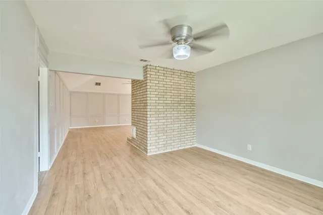 an empty room with wooden floor windows and fan