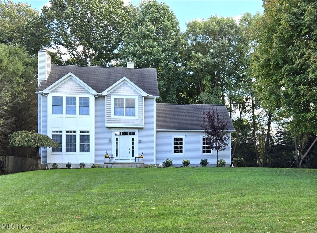 View of front of property with a front lawn, a chimney, view of wooded area, and a shingled roof