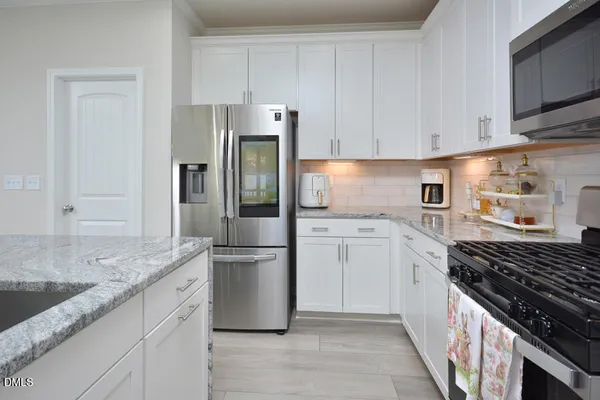 a kitchen with stainless steel appliances kitchen island granite countertop a refrigerator a stove a sink a dining table and chairs with wooden floor