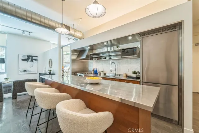 a kitchen with stainless steel appliances granite countertop a sink a stove a refrigerator a dining table and chairs with wooden floor