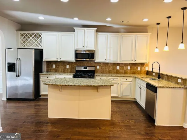 a kitchen with stainless steel appliances granite countertop a stove a sink a refrigerator a microwave and white cabinets with wooden floor