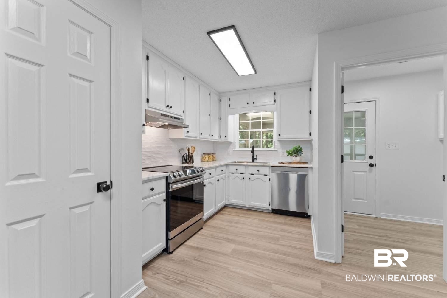 10251 Windmill Road Fairhope, AL 36532 - Photo 25 of 44 Kitchen featuring stainless steel appliances, under cabinet range hood, white cabinetry, light countertops, and light wood-style floors