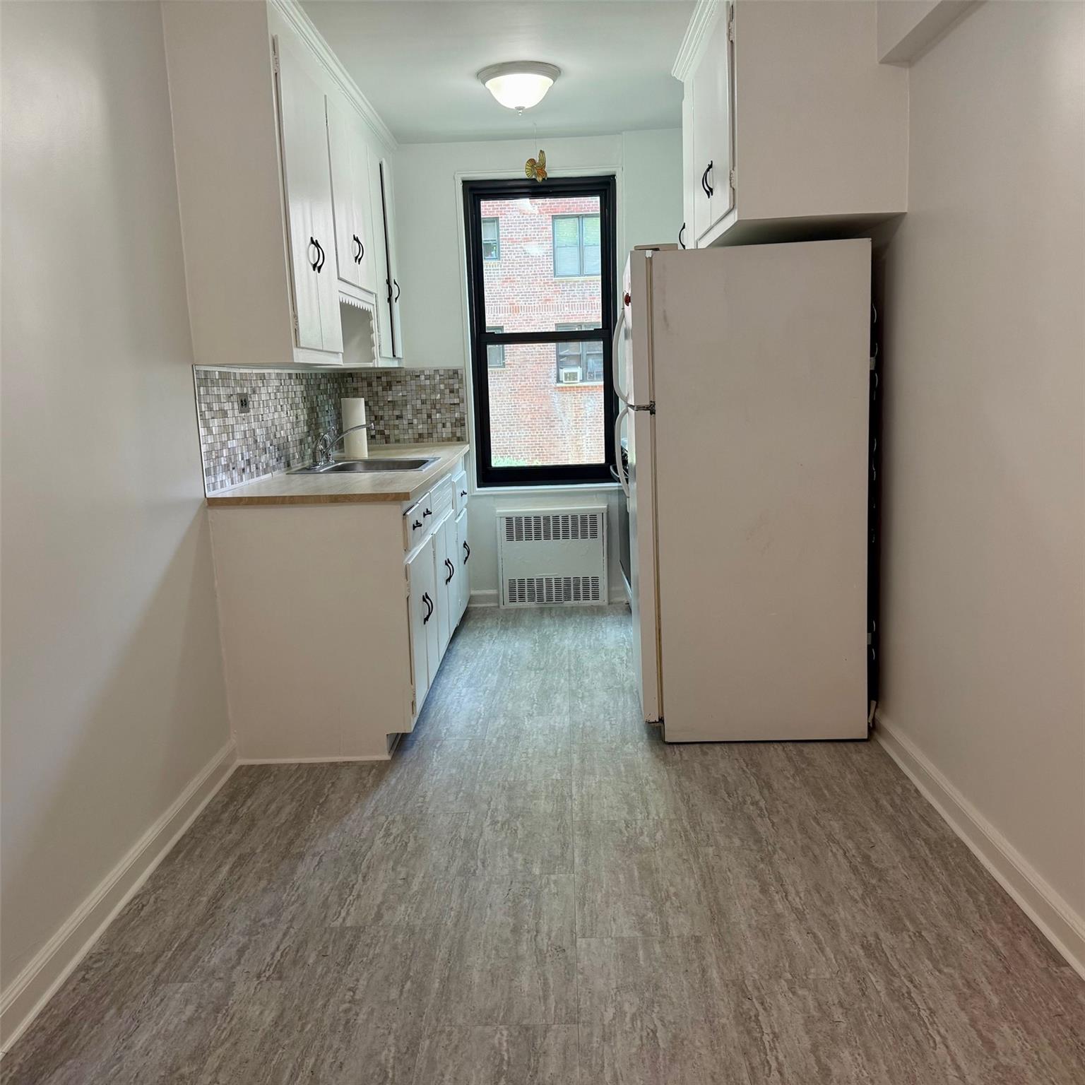 83-20 98th Street, Unit 1H Queens, NY 11421 - Photo 6 of 11 Kitchen featuring freestanding refrigerator, radiator, wood finished floors, white cabinetry, and tasteful backsplash