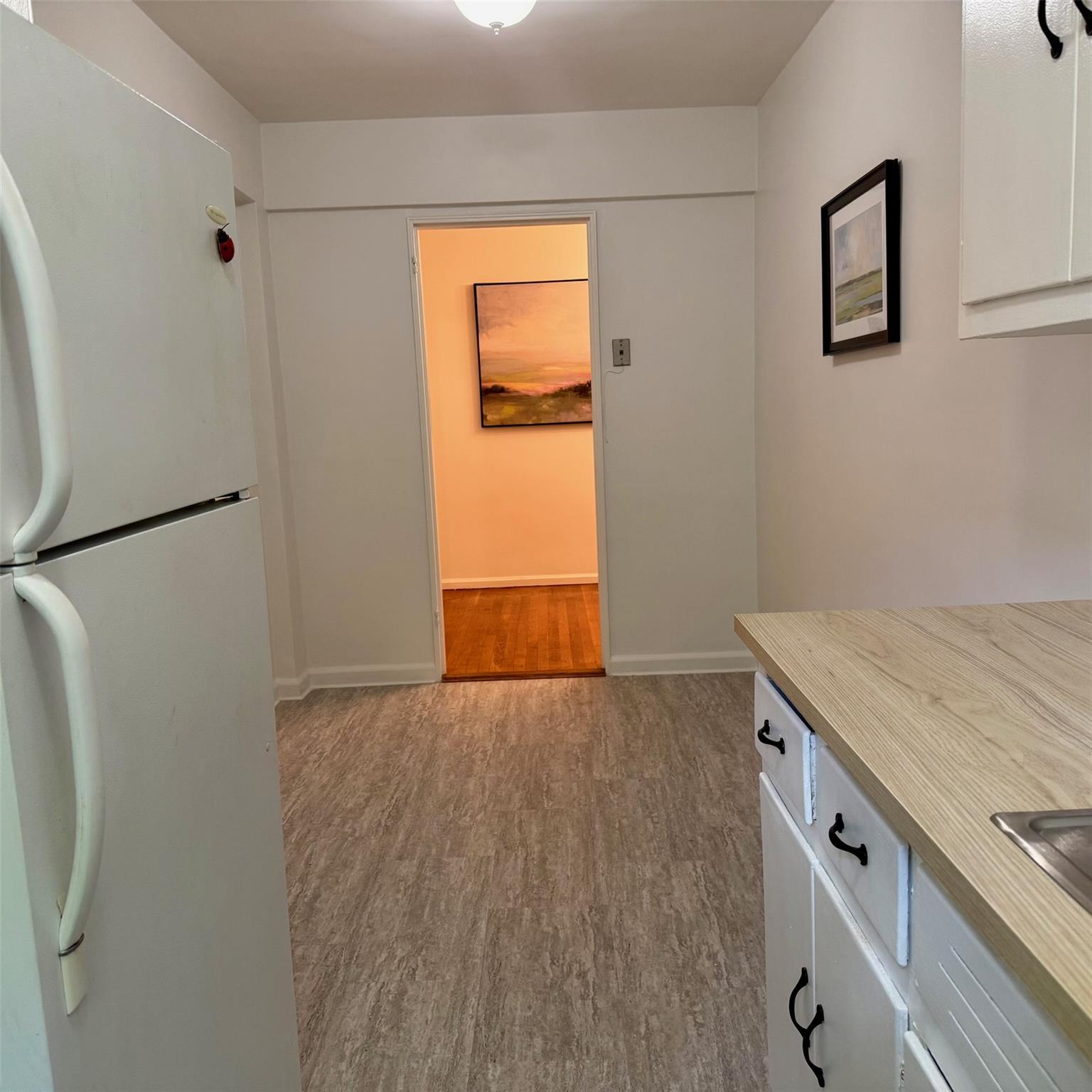 83-20 98th Street, Unit 1H Queens, NY 11421 - Photo 7 of 11 Kitchen with freestanding refrigerator, wood finished floors, light countertops, and white cabinets