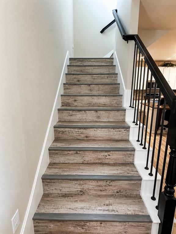 3704 Banton Street Rowlett, TX 75089 - Photo 10 of 16 Staircase featuring wood-finish treads, white risers, and a black wrought-iron railing with a matching newel post