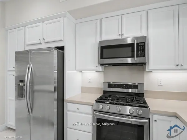 a kitchen with stainless steel appliances granite countertop white cabinets and a stove a refrigerator with wooden floor