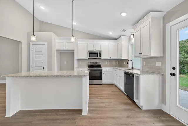 a kitchen with stainless steel appliances granite countertop a refrigerator a sink dishwasher a stove and white cabinets with wooden floor