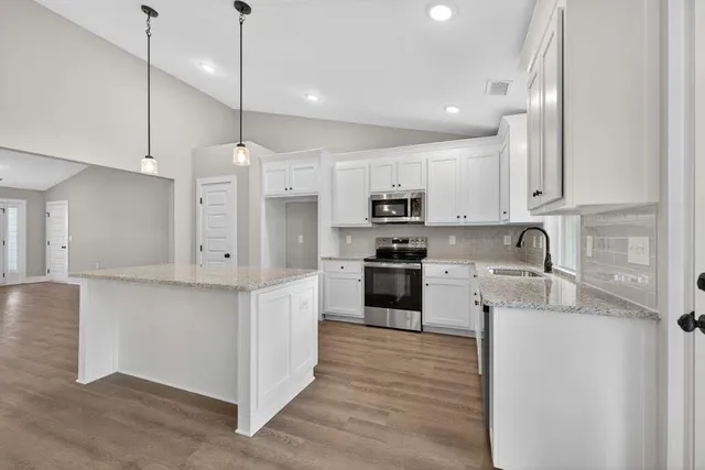 a kitchen with stainless steel appliances granite countertop a sink a stove a refrigerator and white cabinets with wooden floor