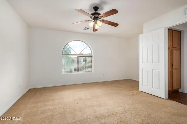 an empty room with chandelier fan and windows