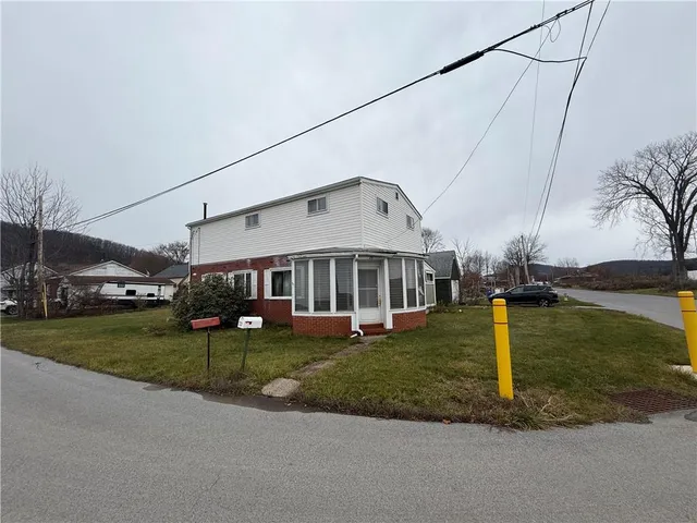 a view of a white house next to a yard with big trees