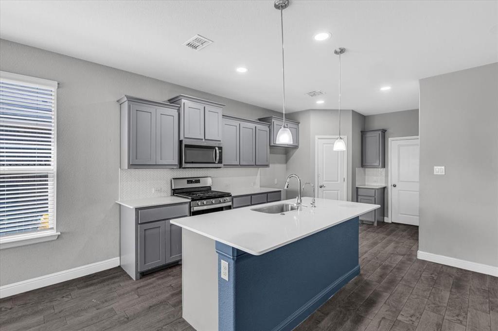 1402 Pleasanton Road Cleburne, TX 76033 - Photo 12 of 36 Kitchen featuring a central island with an undermount sink, pendant lighting, wood-finish flooring, gray cabinetry, and white countertops
