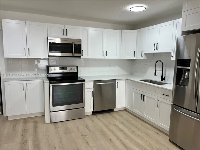 a kitchen with stainless steel appliances white cabinets a sink a stove a microwave and cabinetry