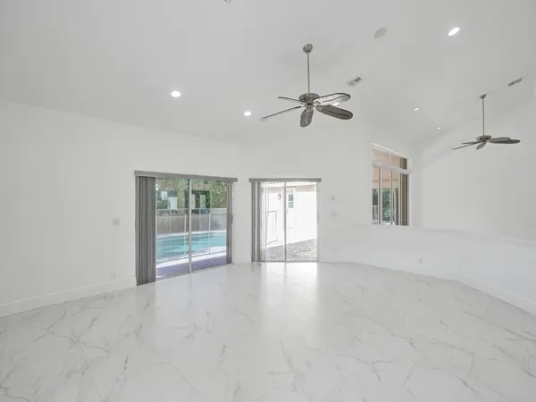 an empty room with chandelier fan and windows