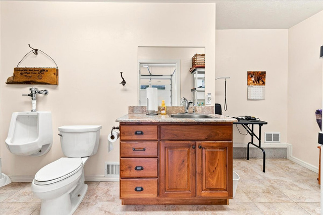 11290 South Southfield Road Mayfield, UT 84643 - Photo 95 of 103 Ceramic tile flooring, white toilet, wall-mounted urinal, wood-finish vanity with stone countertop, and integrated sink