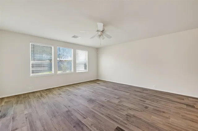 an empty room with wooden floor ceiling fan and windows