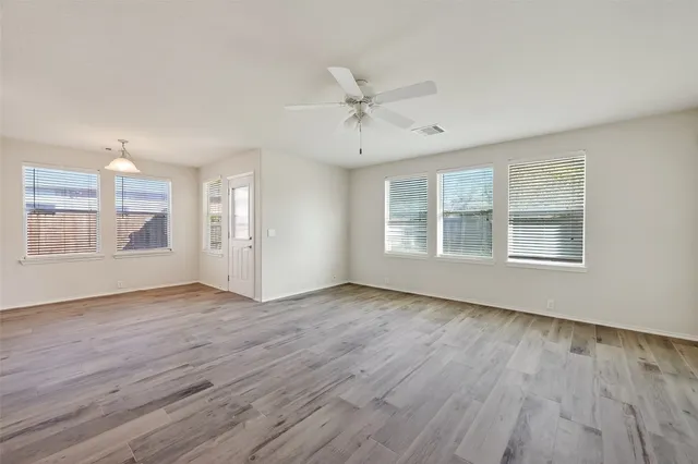 a view of empty room with wooden floor and kitchen